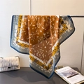 Detail of silk-like scarf with floral prints and navy border draped on a metal rack - Brown