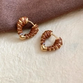 Vue macro de boucles d'oreilles cœur en or 18k avec cuir marron sur tissu doux - Marron