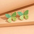 Green raffia woven butterfly earrings with gold frame on warm orange stand - Green