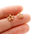 Macro shot of gold hollow star stud earrings on fingertips showing small size and detail - Gold