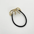 Detail van zwarte haarelastiek met een elegante gouden metalen strik decoratie - Goud