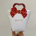 Detail of white gift bag with red polka dot bow and merci beaucoup French typography - Hand-held Card + Two-legged Pin
