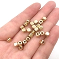 Makroaufnahme von goldenen Würfel-Zwischenperlen in der Hand für DIY-Schmuckherstellung - Quadratische Zwischenperlen Gold 4mm (2000 Stk)