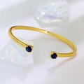 Minimalist 18K gold-plated open bangle with two blue round zircon stones on white texture - Copper Plated 18K Gold / Gold with Double Blue Zirconia