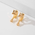 Elegante goldene Ohrringe mit quadratischen Steinen und Tropfenanhängern auf Weiß - Champagner