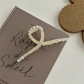 Dettaglio di una grande molletta per capelli in acetato crema con perle su un libro - Pinza a Squalo in Lega con Perle