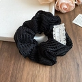 Detail eines schwarzen Falten-Scrunchie aus Spitze mit feiner Textur und weißem Etikett - Schwarz