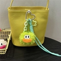 Close-up of a green plush monster charm on a yellow leather bucket bag with silver clip - Green