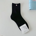 Flach liegende schwarze Socken mit rosa Zierknopf und Baumwolletikett auf Weiß - Einheitsgröße / Schwarz