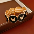 Primer plano de pulsera de mariposa esmaltada en oro y negro con banda elástica - Mariposa Negra Dorada