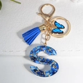 Detail of blue resin letter S keychain with gold butterfly charm and tassel on white leather - Letter S