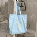 Detail of light blue canvas tote bag with yellow embroidered text on glass door handle - Light Blue
