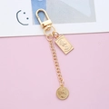Macro detail of golden keychain with Queen Elizabeth II coin charms on pink background - Round Plate Buckle