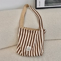 Détail d'un sac cabas en toile rayée avec étiquette de marque sur fond de canapé beige - Bandoulière simple / Rayures Brunes