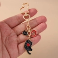 Detail of golden metal keychain featuring black cat silhouettes and red heart charms - Red Heart Cat