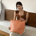 Handwoven orange straw tote bag for summer vacation held by a model on a wooden bench - Large / Orange