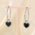 Detalle de pendientes de aro plateados con colgante de corazón de esmalte negro en soporte - Pendientes de Aro Trenzados con Corazón / Acero y Corazón Negro
