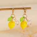 Detailed view of yellow lemon earrings with green leaf and white bead on a gold stand - Lemon Stud Style (0916)