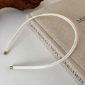 Primer plano de diadema fina de cuero blanco con puntas doradas sobre una base de madera rústica - crema
