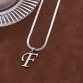 Silver F letter pendant necklace with sleek flat snake chain on a brown velvet base - Letter F