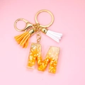 Detail of letter M resin keychain with orange stones and yellow white tassels - M