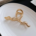 Dettaglio della molletta per capelli ondulata in metallo dorato su piatto di ceramica - Oro