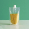 Sacchetto trasparente con beccuccio in plastica riempito di chicchi su sfondo verde - Capacità 500g / Beccuccio Dritto