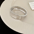 Dettaglio di un ampio bracciale rigido in metallo argento con superficie lucida e cerniera - Stile Lucido Ovale / Argento