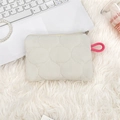 Quilted cream cosmetic pouch with pink knotted handle shown in cozy lifestyle setting - Cream