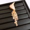 Dettaglio di una spilla a nappa geometrica dorata con pendenti a foglia su sfondo nero - Oro - Grande