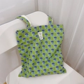 Détail du sac cabas en toile verte avec motifs floraux mauves et étiquette texte - Le magicien d'Oz vert
