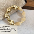 Macro shot of gold and beige acrylic bead bracelet on a textured fabric backdrop - Bracelet / White