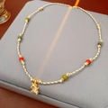 Dettaglio di collana vintage con perline colorate e un ciondolo a forma di animale dorato - Collana-Oro-Multicolore-Rosa