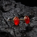 Macro detail of oval red carnelian stud earrings with gold finish on a dark texture - Natural Red Agate Oval Gold 5*7mm