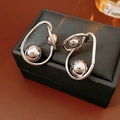 Macro shot of silver metallic twisted hoop earrings with spherical beads on black box - Silver