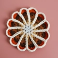 Handgehaakte bloem onderzetter met blauw midden en warm verloop op een roze achtergrond - Nr. 6 Verloop