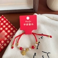 Rotes geflochtenes Armband mit goldenem Kalbsanhänger und Perlen auf Geschenkkarte - Goldener Ochse Rotes Geflochtenes Armband
