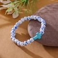 Beaded bracelet with blue-spotted white stones and a turquoise cross on kraft paper - White Blue Spotted Blue Green Cross Bracelet