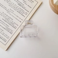 Close-up of a clear square hair claw clip with golden metal spring on a book - Glossy Transparent White