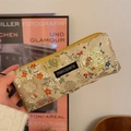 Close-up of floral embroidery texture and black logo patch on a beige fabric pouch - Mud Gold