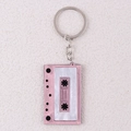 Close-up of pink and white tape cassette keychain with Friends text on beige texture - Pink
