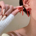 Detail of red bow stud earrings with glossy finish on model with white knit sweater - Wine Red Slender Bow Knot (11788)