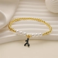 Pulsera de perlas doradas con colgante de coral negro sobre fondo de seda elegante - Negro