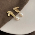 Detailed close-up of golden leaf earrings with white teardrop pearls on a ceramic dish - Style 23