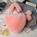 Detail of pink faux fur heart bag with golden chain and plush ball charms on denim - Pink