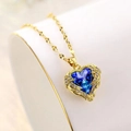 Elegante collana dorata con pendente a cuore di cristallo blu e ali su uno sfondo morbido - Cristallo Blu Oro
