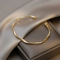 Dettaglio di bracciale rigido dorato a torsione con sfere lucide su seta elegante - Bracciale Rigido Geometrico Intrecciato (HB637) / Oro