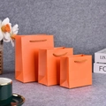 Three orange gift paper bags in various sizes with matching cord handles on a desk - Pearlescent Orange