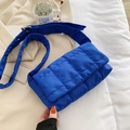 Blue quilted nylon puffer shoulder bag with adjustable strap on a minimalist soft bed - Light Blue