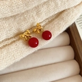 Detailed close-up of red bow and gold sphere earrings on a cream velvet tray - Bow Tie Resin Red Ball Pendant Studs